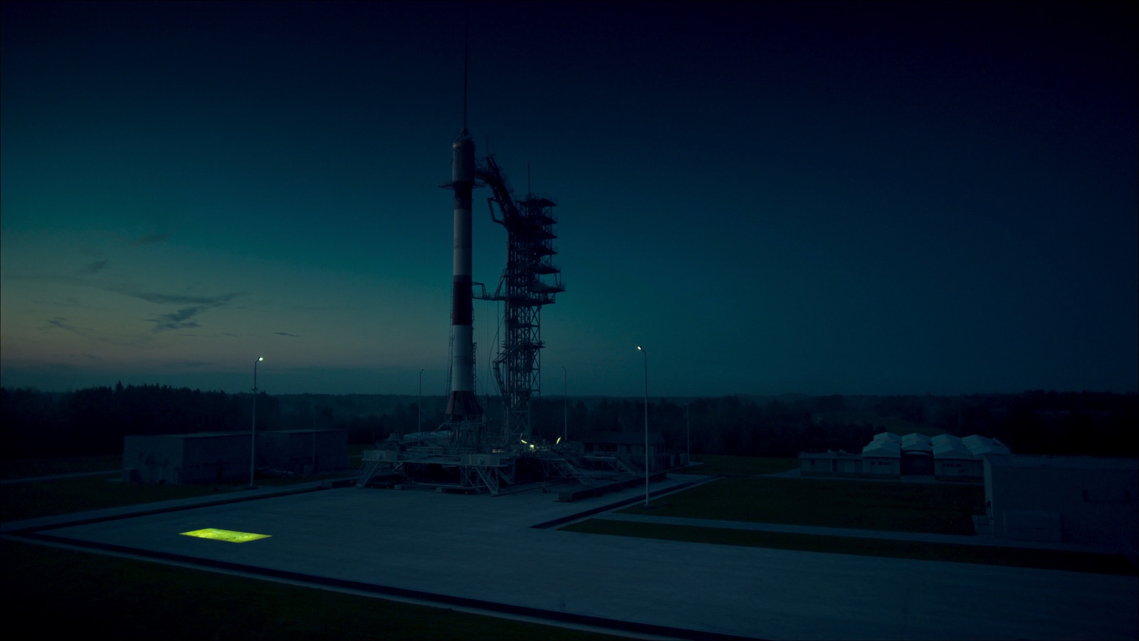 A launch vehicle standing on the pad at dusk, a single chartreuse marking on the apron