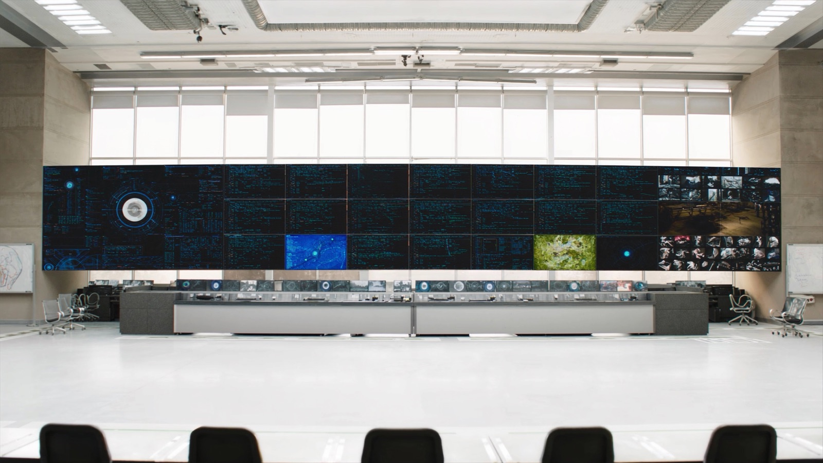 Mission operations control room — consoles and wall screens monitoring multiple missions